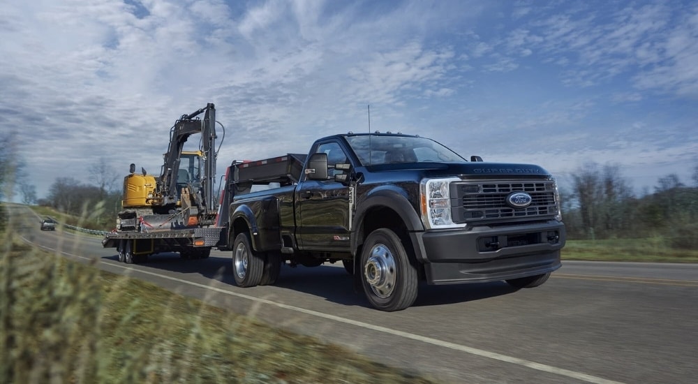 A black 2025 Ford F-450 XL is shown towing construction equipment.