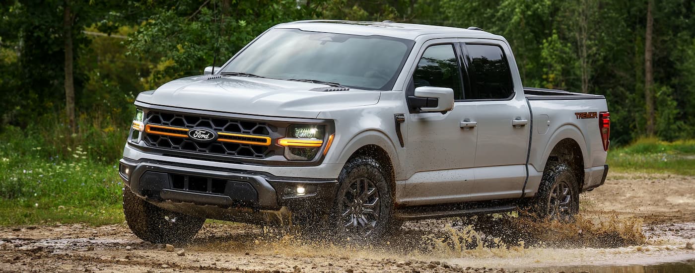 A grey 2025 Ford F-150 Tremor off-roading through mud in the woods.
