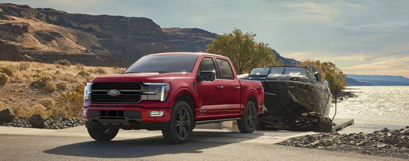 A red 2025 Ford F-150 Platinum towing a boat at a lake.