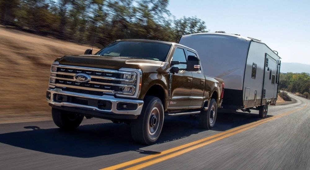 A brown 2025 Ford F-250 Tremor towing a camper on an open road.