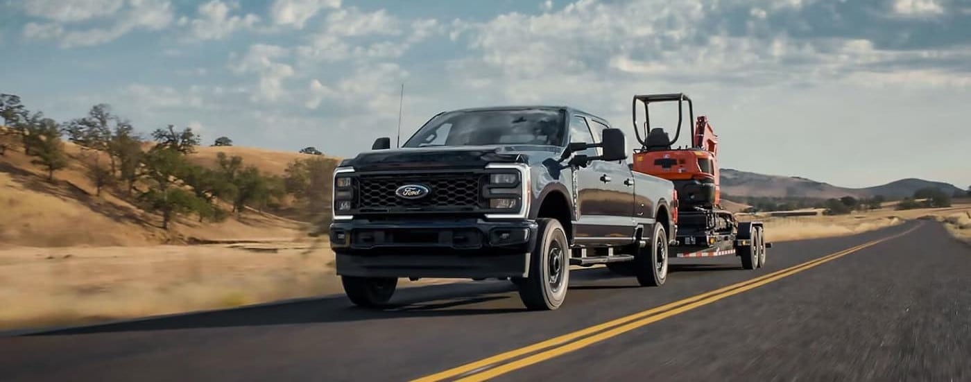 A black 2025 Ford F-350 for sale is shown towing a trailer on a highway.
