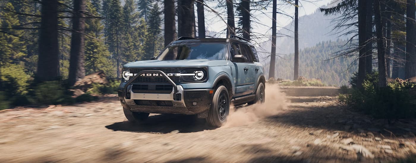 Blue 2025 Ford Bronco Sport Outer Banks driving on a dirt road in the woods