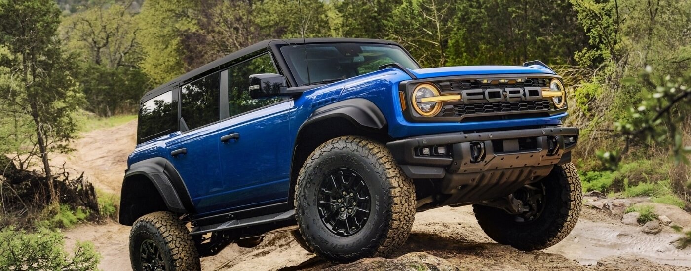 A blue 2025 Ford Bronco Raptor off-roading through the woods.