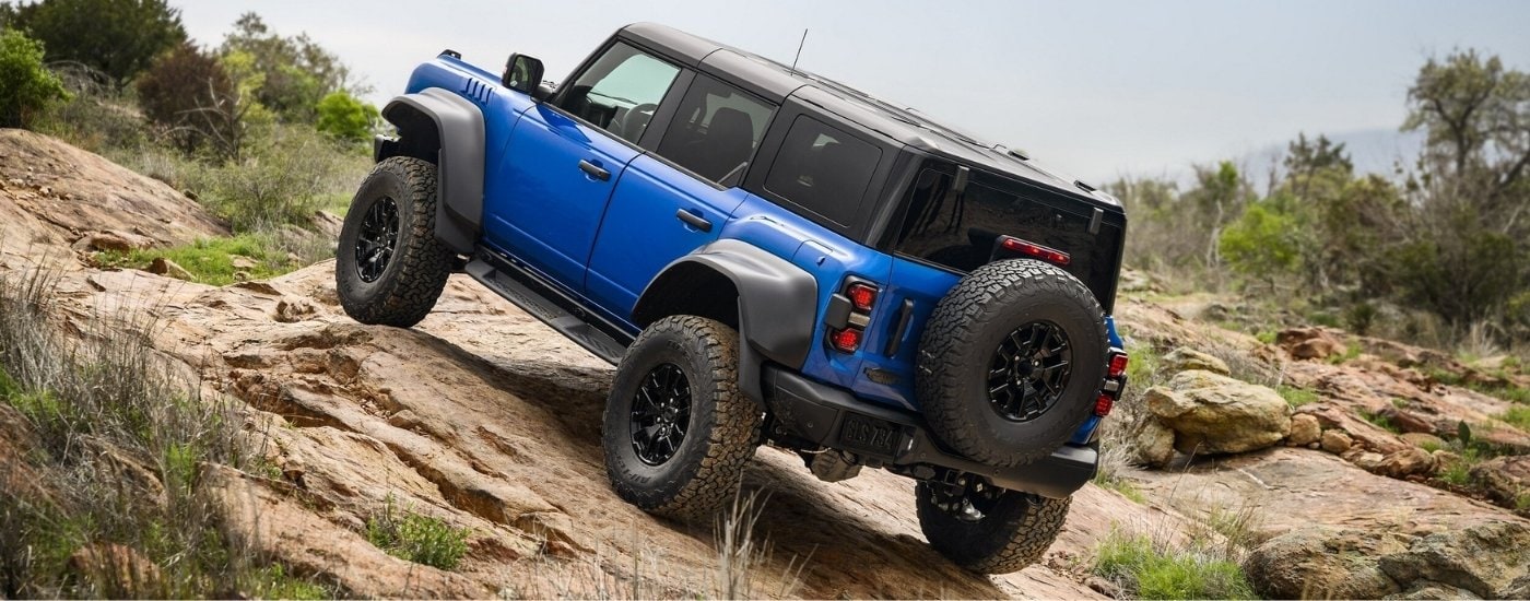 A blue 2025 Ford Bronco Raptor is shown from the rear off-road.