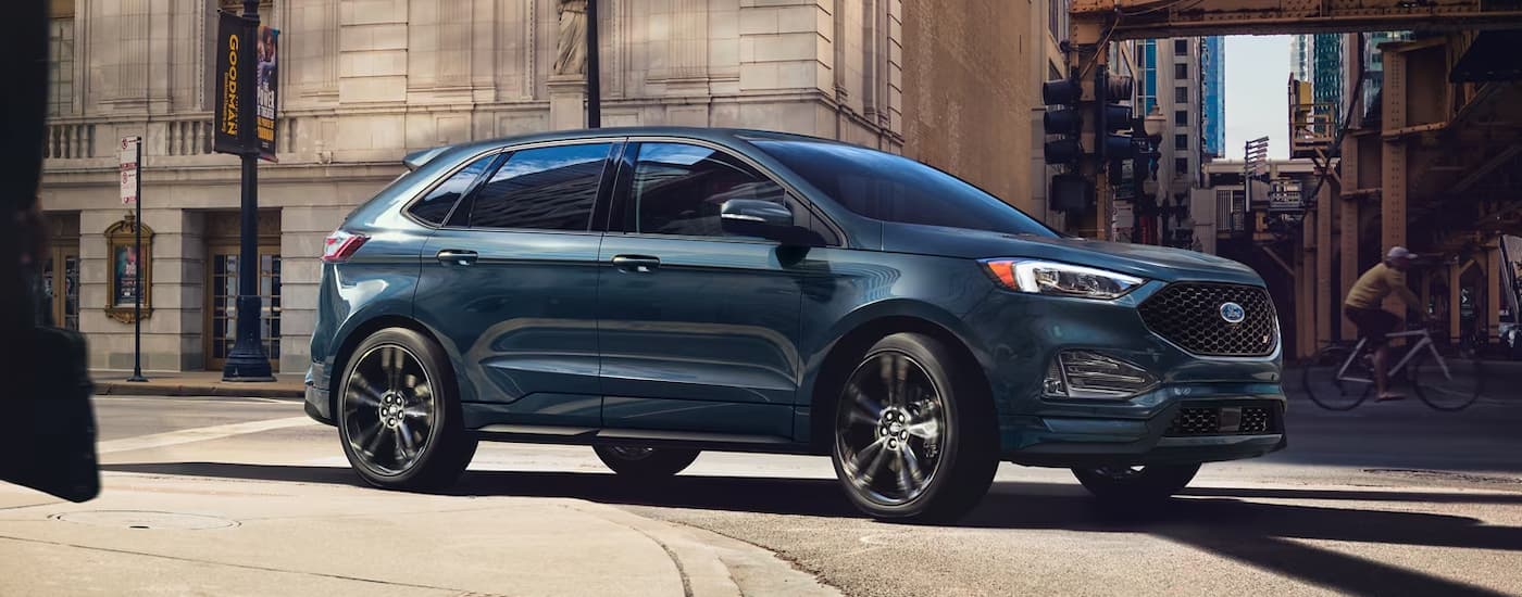 A blue 2024 Ford Edge ST driving to a Ford dealer.