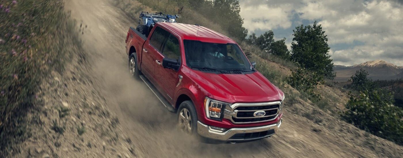 A red 2023 Ford F-150 driving off-road down a rocky hill.