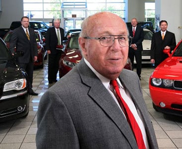 Man standing in front of four other men and vehicles in a Nissan showroom