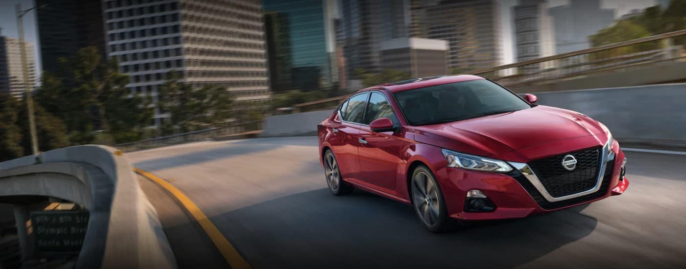 A red 2021 Nissan Altima is shown from the front at an angle after leaving a dealer that has a used Nissan for sale.
