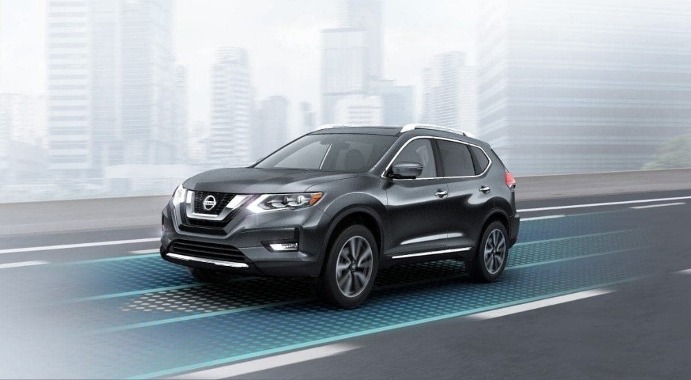 A grey 2020 Nissan Rogue driving past a city.