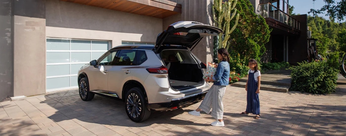 A woman using the motion activated liftgate of a white 2025 Nissan Rogue Platinum parked in the driveway.