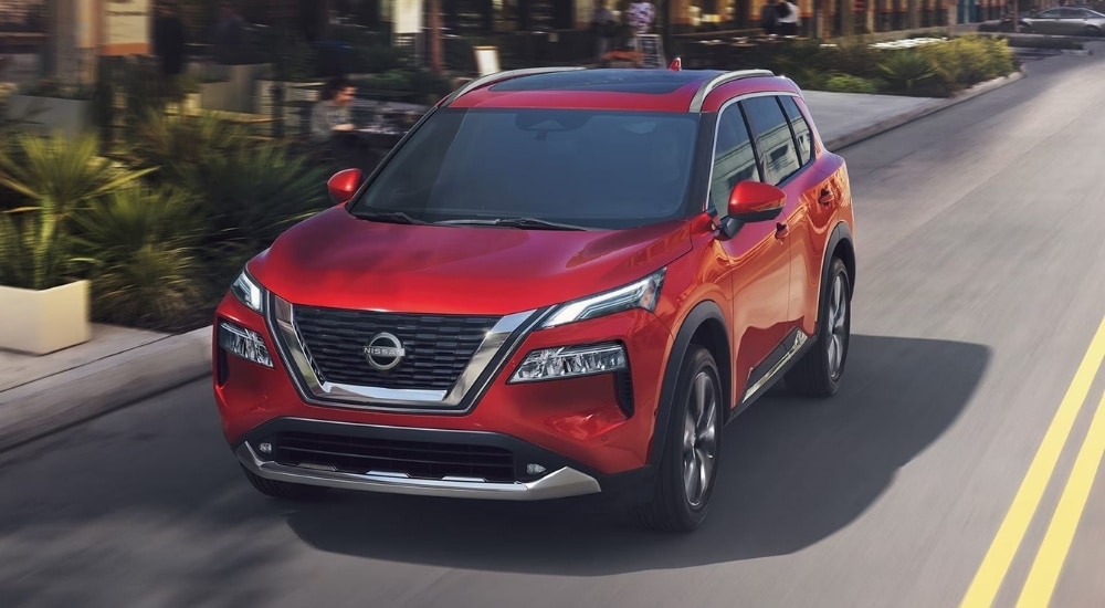 A red 2023 used Nissan Rogue for sale driving on an open road.