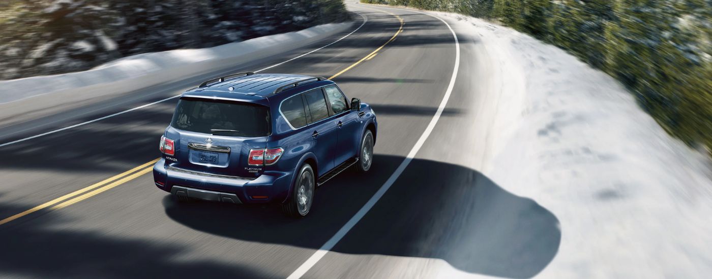 Rear view of a blue 2020 Nissan Armada Platinum driving down a bending road.