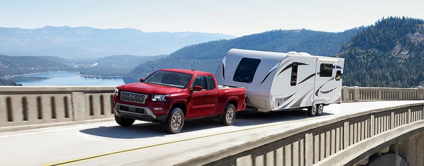 A red 2024 Nissan Frontier is shown towing a trailer on a bridge.