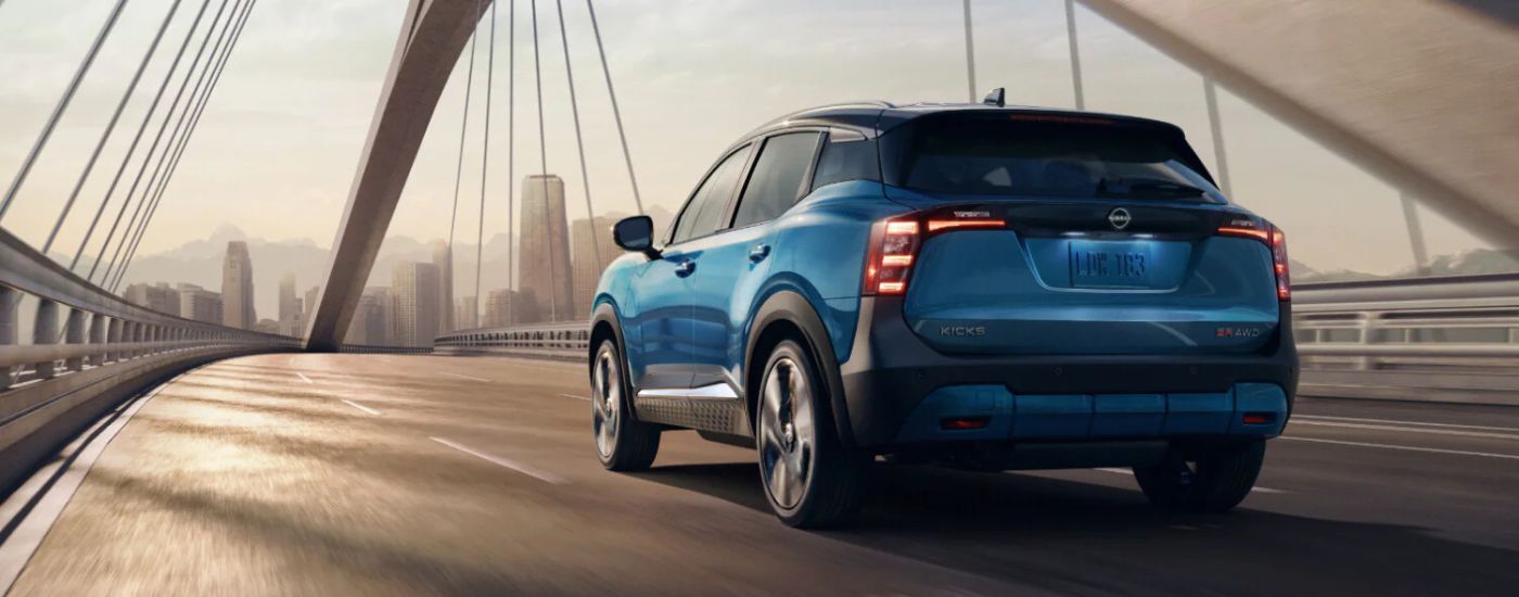 Rear view of a blue 2025 Nissan Kicks SR driving over a bridge.