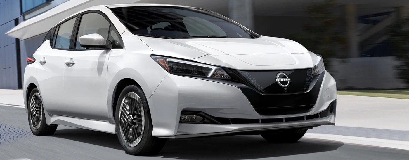 A white 2023 Nissan Leaf driving from a dealer with a used Nissan for sale near Celina.