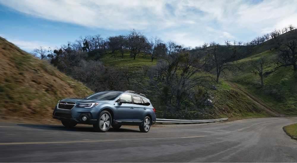 A blue 2018 Subaru Outback 50th Anniversary Edition is shown driving on a cloudy day.