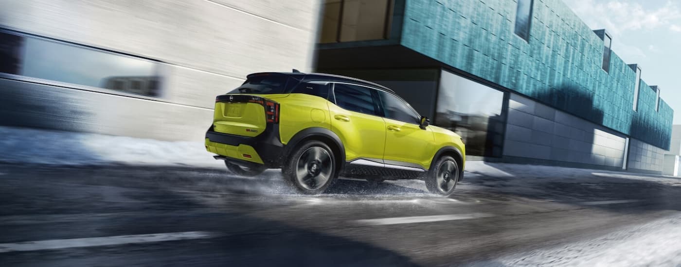 Rear of a yellow 2026 Nissan Kicks SR driving down a road.