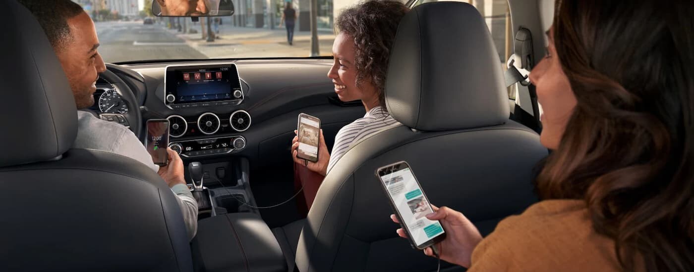 People holding cellphones in the black interior in a 2025 Nissan Sentra.