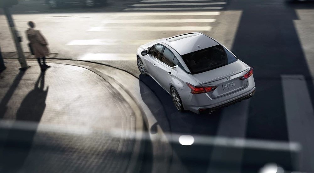 High rear angle view of a white 2023 Nissan Altima driving around a bend.