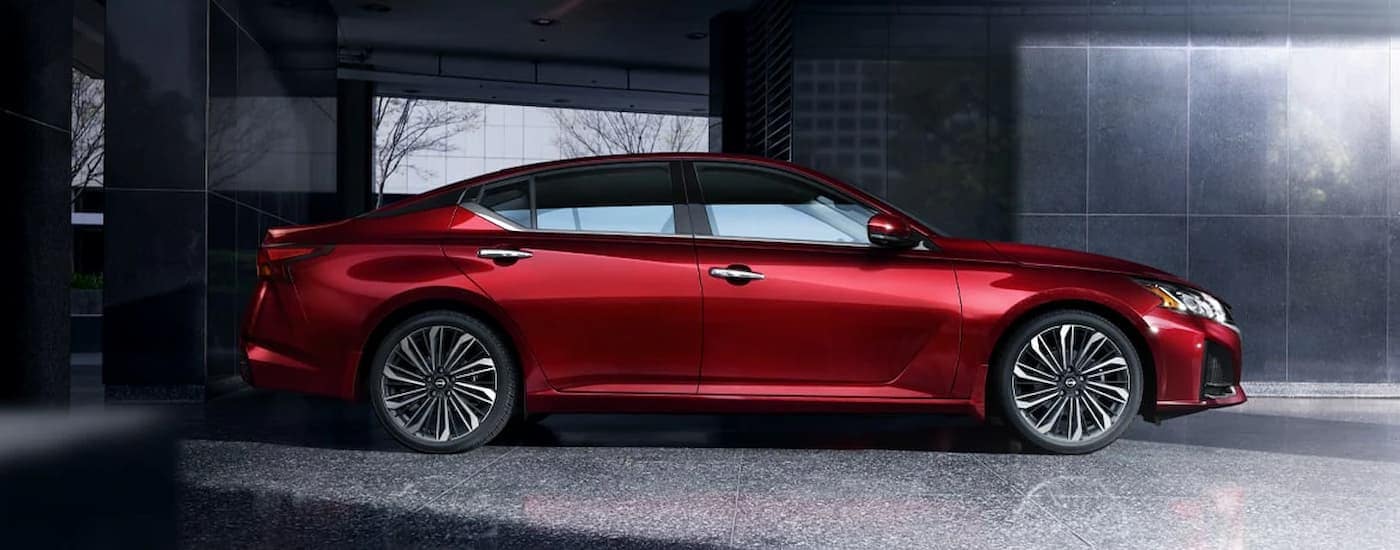A side view of a red 2024 Nissan Altima parked in a city at night.