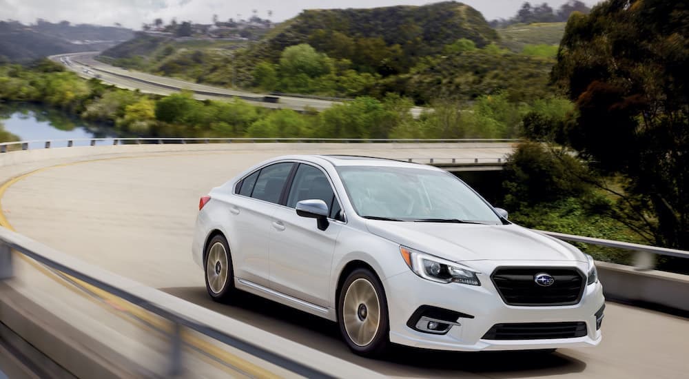 A white 2021 Subaru Legacy is shown driving down a winding bridge after leaving a Subaru Legacy dealer.