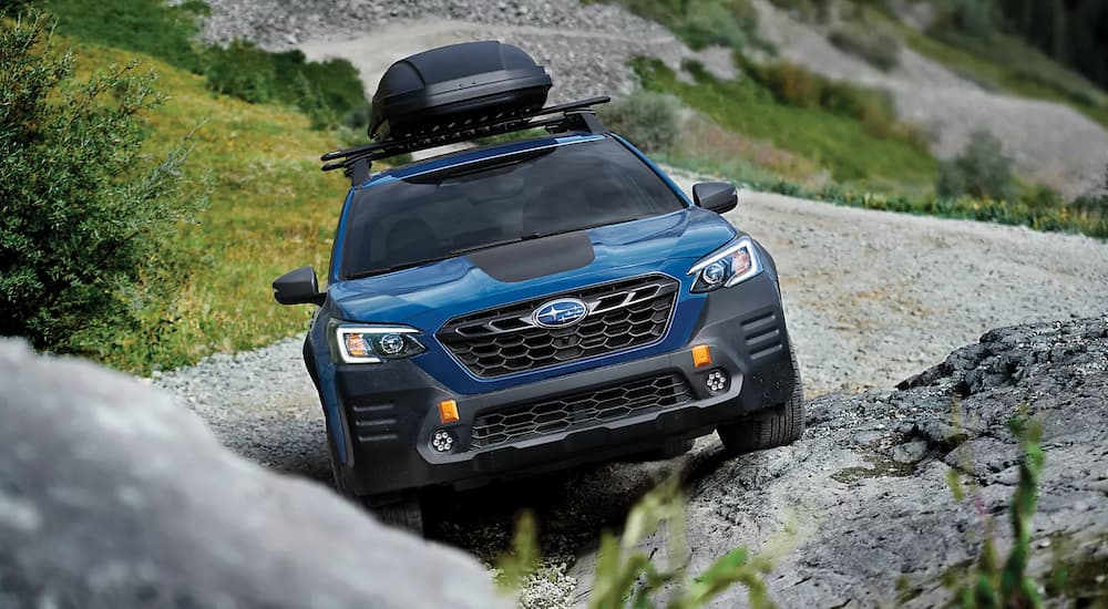 A blue 2023 Subaru Outback is shown from the front off-roading on a steep hill.