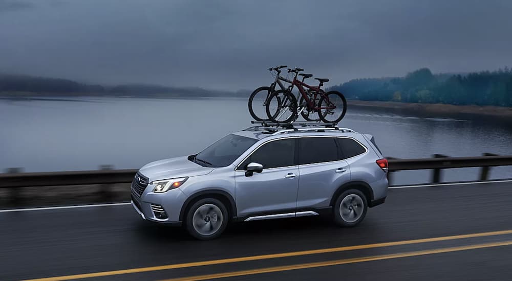 A white 2023 Subaru Forester Touring is shown driving on an open road.