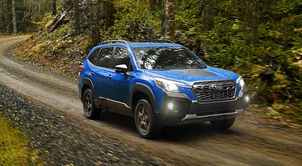 A blue 2022 Subaru Forester Wilderness is shown from the side driving on a dirt road in the forest after leaving a New Jersey Subaru dealer.