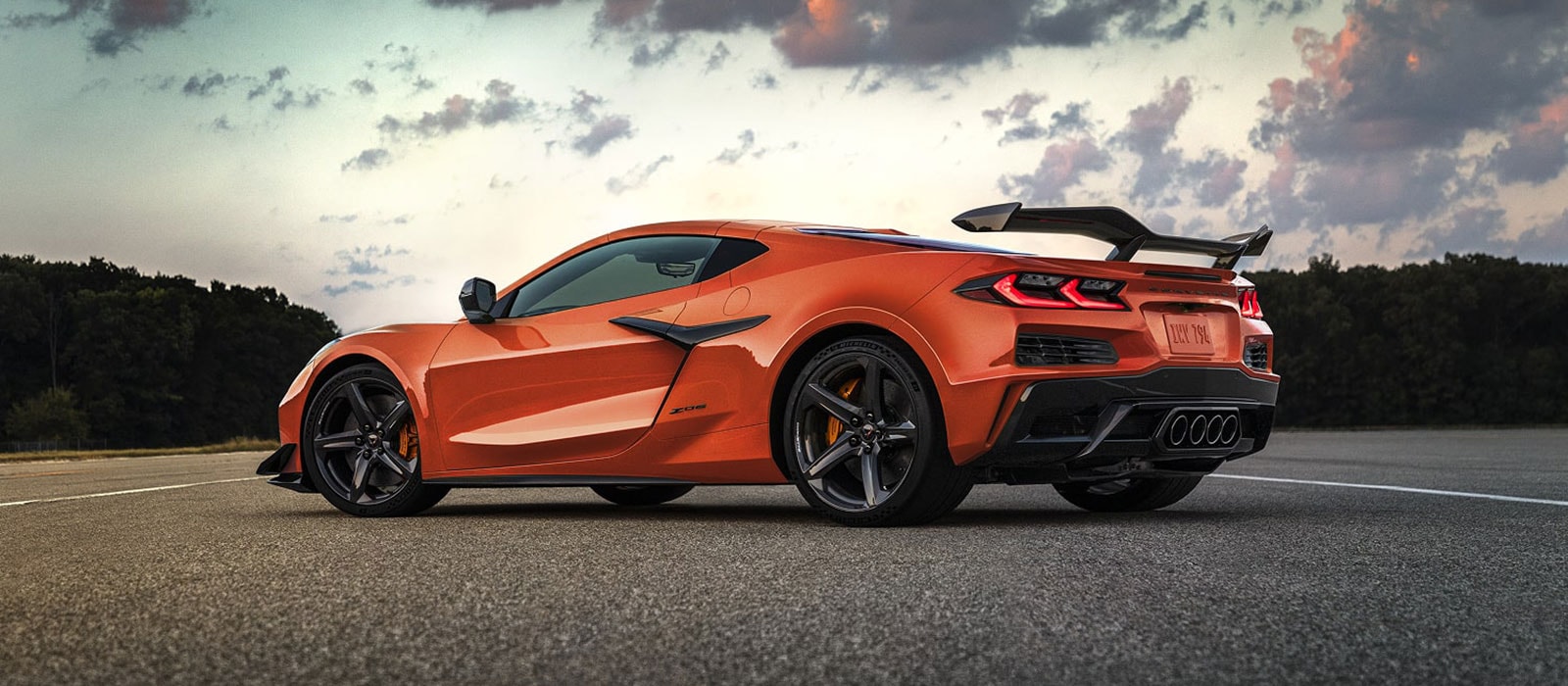 An orange Chevrolet Corvette in profile, parked in the middle of a road.