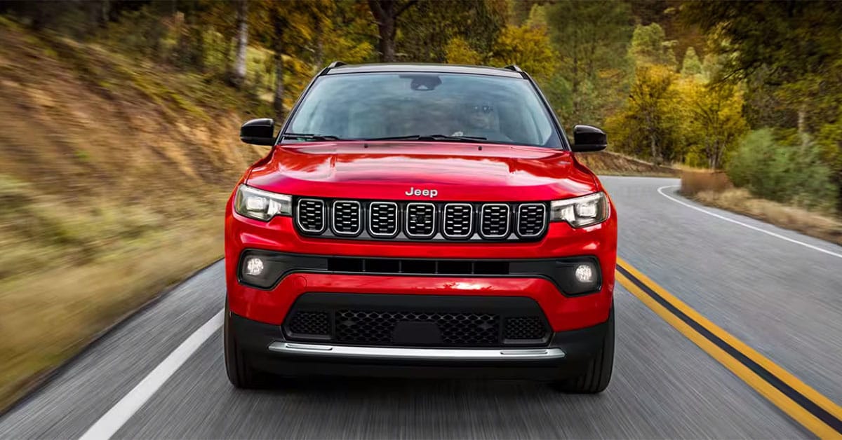A red 2025 Jeep Compass driving on a winding paved road