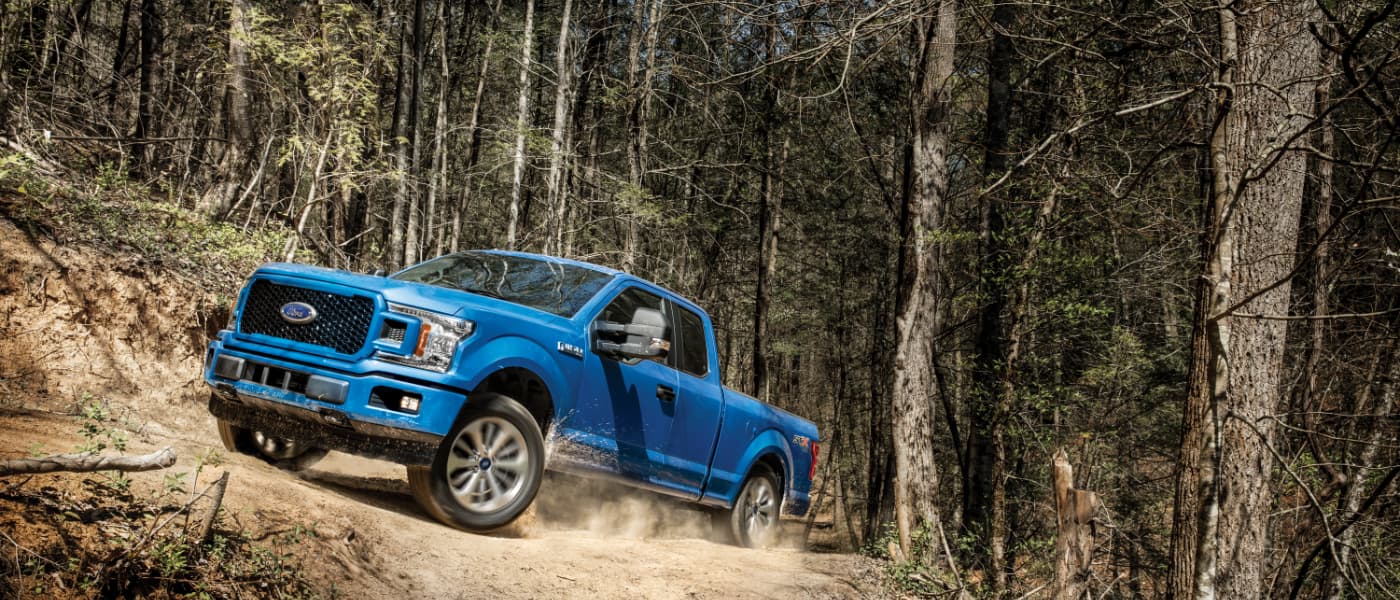 2020 Ford F-150 in blue driving up hill while off road in a forest