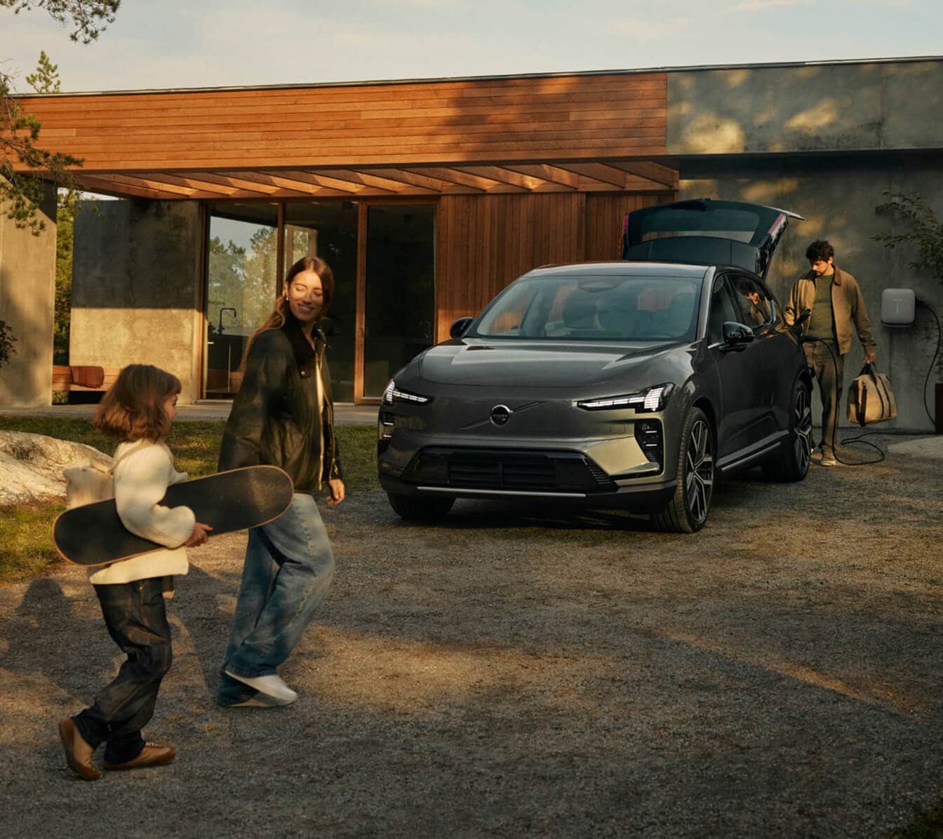 Exterior view of a dark gray Volvo XC60 parked in a driveway with a family walking nearby.