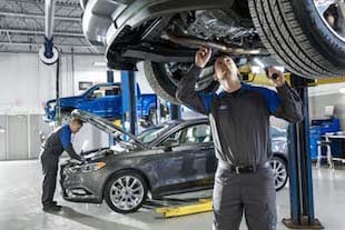 A Ford Service Technician working under a car in a body shop