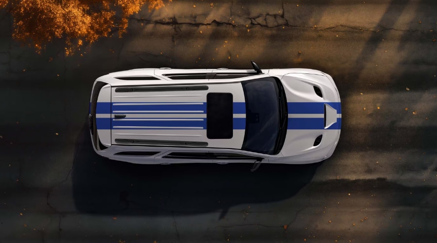 Overhead top-down view of a white 2026 Dodge Durango with blue racing stripes driving on an asphalt street scattered with autumn leaves, highlighting AWD stability on slick backroads in East Brunswick and Old Bridge NJ.