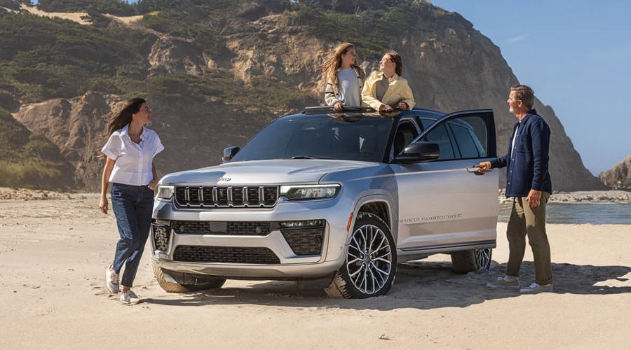Family enjoying a weekend trip with a silver 2026 Jeep Grand Cherokee on the sand, highlighting Selec-Terrain Mud/Sand mode for Jersey Shore and Monmouth County drives from East Brunswick, NJ.