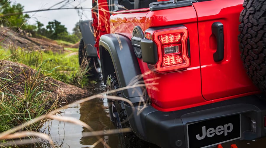 Rear view of red 2026 Jeep Wrangler navigating a muddy trail, highlighting off-road capability for drivers in East Brunswick, NJ, at Route 18 Autos