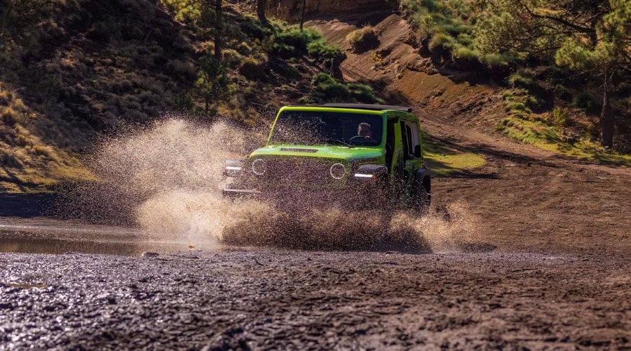 A lime green 2026 Jeep Wrangler splashing through a water crossing on an off-road trail, showcasing the rugged performance available at Route 18 Autos in East Brunswick, NJ