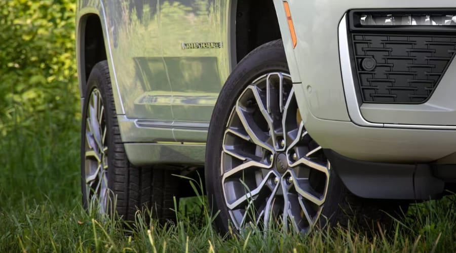Close-up of alloy wheels and all-season tread on a 2026 Jeep Grand Cherokee parked on grass, highlighting tire pressure monitoring and wet-road traction for autumn commutes across East Brunswick and Middlesex County, New Jersey.