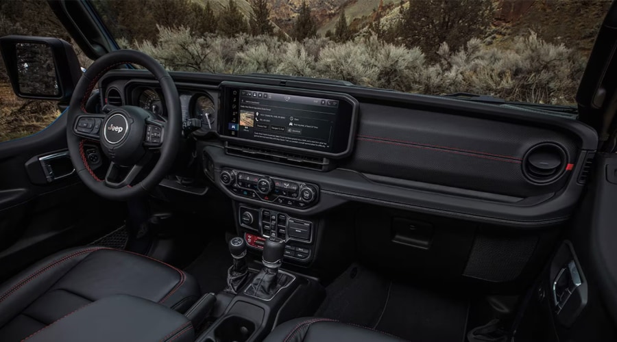 Full cabin interior view of a 2026 Jeep Wrangler showing premium leather seats with red accent stitching, leather-wrapped steering wheel, 4x4 gear shifters, and central touchscreen display, highlighting cold-weather comfort and features at Route 18 Autos in East Brunswick, NJ.