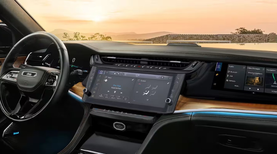 Panoramic view of the 2026 Jeep Grand Cherokee interior dashboard featuring the 10.1-inch Uconnect 5 central touchscreen, front passenger interactive display, wood trim, and McIntosh audio system for East Brunswick and Edison, NJ drivers.