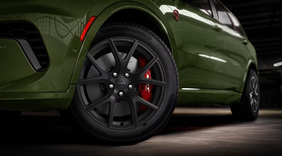 Close-up view of the matte black SRT alloy wheel and red Brembo brake caliper on an olive green 2026 Dodge Durango, highlighting active Rain Brake Support performance for fast stops in East Brunswick NJ.