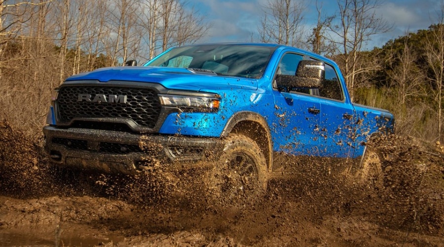 Blue 2026 Ram 1500 truck splashing through deep mud, highlighting the need for routine radar sensor maintenance and camera cleaning at Route 18 CJDR near Edison and East Brunswick, NJ.