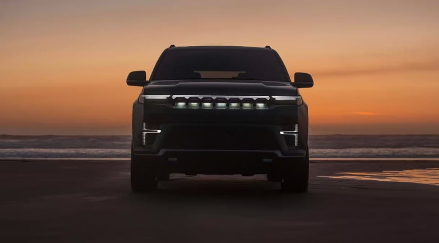 Front silhouette of the 2026 Jeep Grand Wagoneer luxury SUV with illuminated grille and LED headlights at sunset on a coastal beach, available at Route 18 Autos in East Brunswick, NJ.