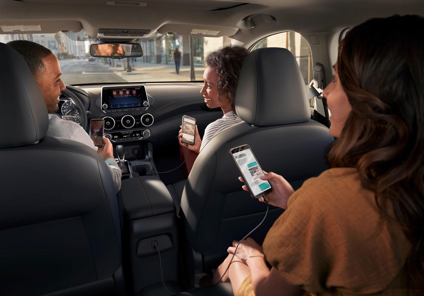 Three people charging their phones in a Nissan Sentra
