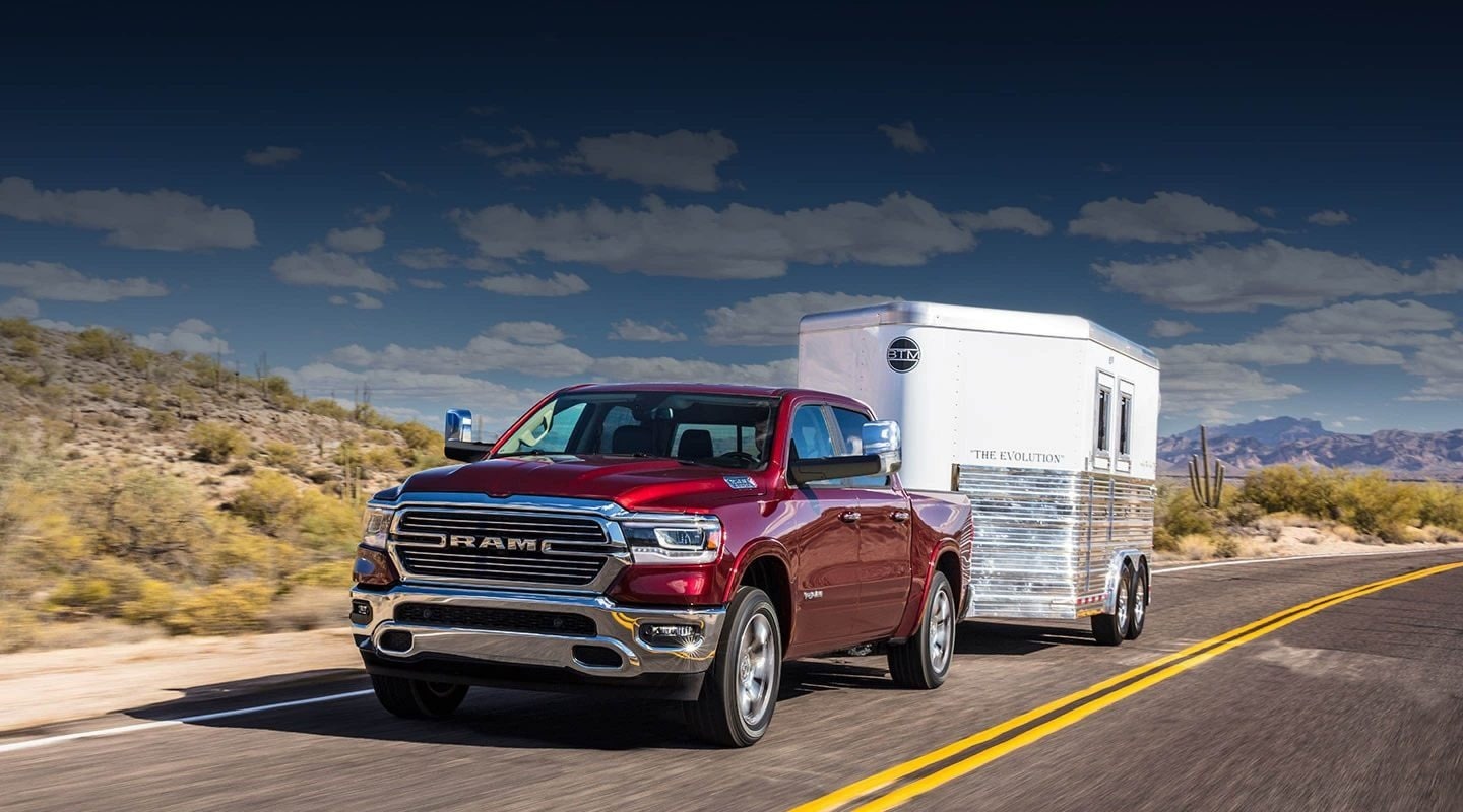 Red RAM truck hauling a small trailer and driving in a desert area