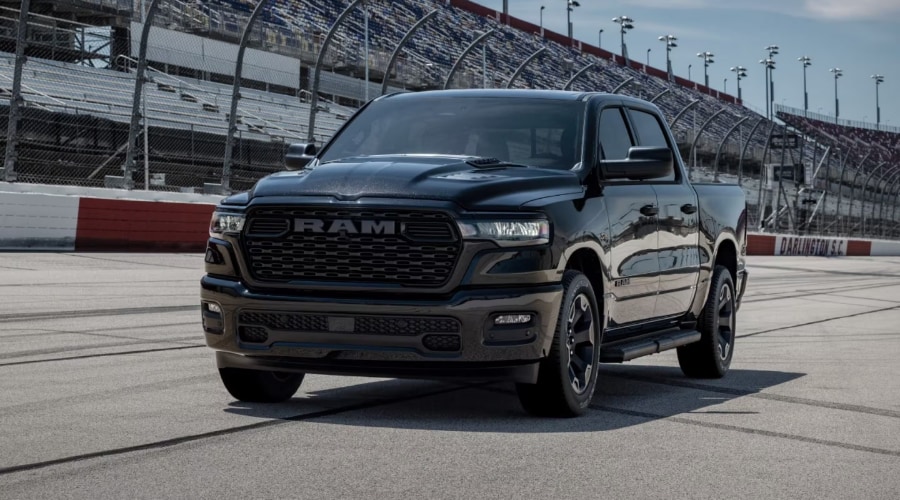 Front three-quarter view of a dark metallic 2026 Ram 1500 pickup truck featuring a bold blacked-out grille, active LED headlights, and Active-Level Four-Corner Air Suspension stance, ready for wet weather driving on I-78 near Summit, NJ.