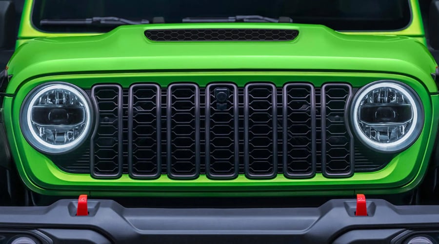 Lime green 2026 Jeep Wrangler front grille highlighting the center-mounted integrated trail camera lens, circular LED halo headlights, and hood scoop, illustrating trail camera setup for Springfield and Summit NJ drivers.