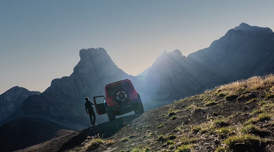 A 2026 Jeep Wrangler parked against a majestic mountain backdrop during an autumn road trip from Summit, NJ, highlighting outdoor adventure capability and weather-ready durability.