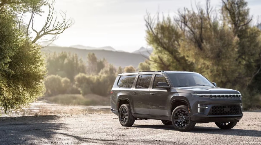 A dark gray 2026 Jeep Grand Wagoneer parked on an unpaved path next to a scenic lake, showcasing its Quadra-Lift Air Suspension capability for drivers in East Brunswick, NJ.