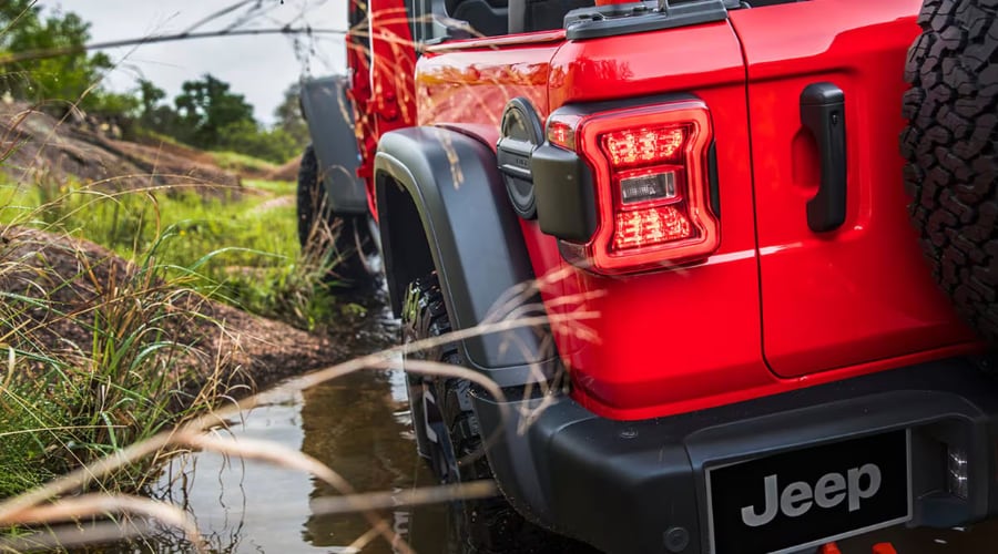 Rear exterior view of a red 2026 Jeep Wrangler navigating wet trails, showcasing wash-out floor drain capabilities and weatherproofing protection for autumn driving in Morris County, NJ.